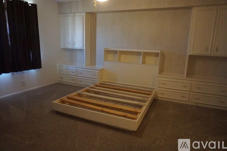 A bed with wooden slats is in a room with white cupboards.