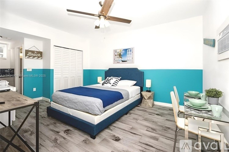 A bedroom with a bed, a dining table, and a ceiling fan.