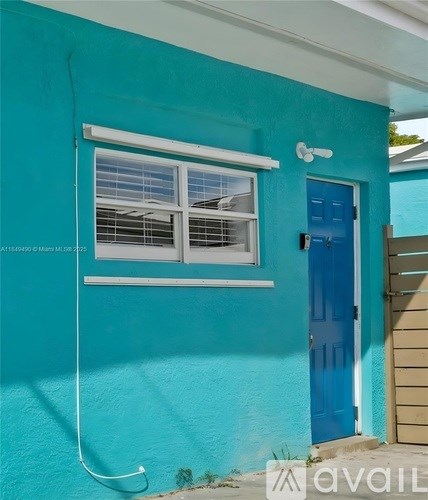 A blue door is on the right side of a white window on a blue wall.