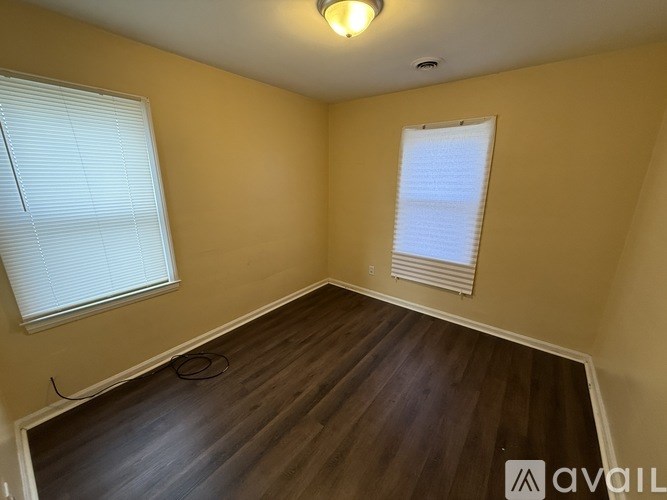 A room with wooden flooring and two windows with blinds.