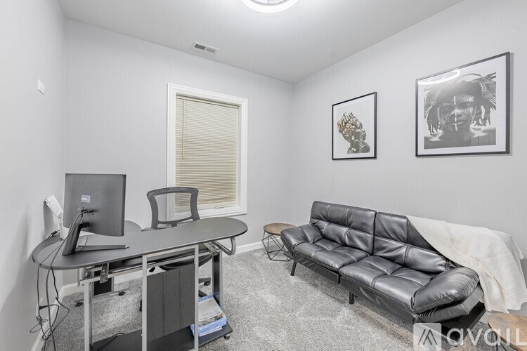 A black leather sofa sits in a white room with a desk and computer.