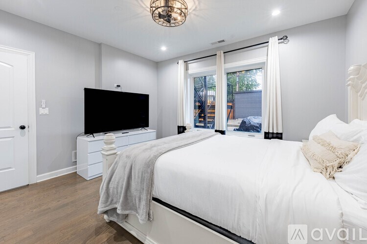 A bedroom with a large bed, a television, and a window with curtains.