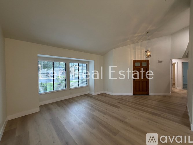 A spacious room with wooden flooring and a large window with blinds.