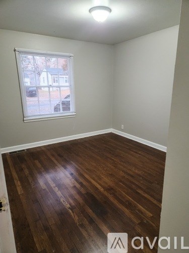 A room with wooden flooring and a window showing a view of a building outside.