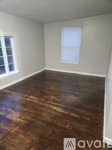 A room with wooden flooring and two windows.