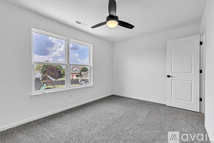A room with a ceiling fan and a window showing a view of houses and trees.
