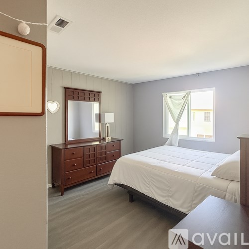 A bedroom with a large bed, a dresser with a mirror, and a window with curtains.