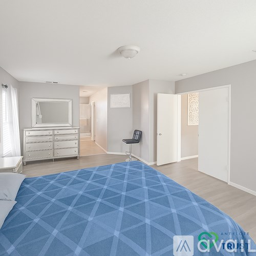 A bedroom with a blue bedspread and a white chair.