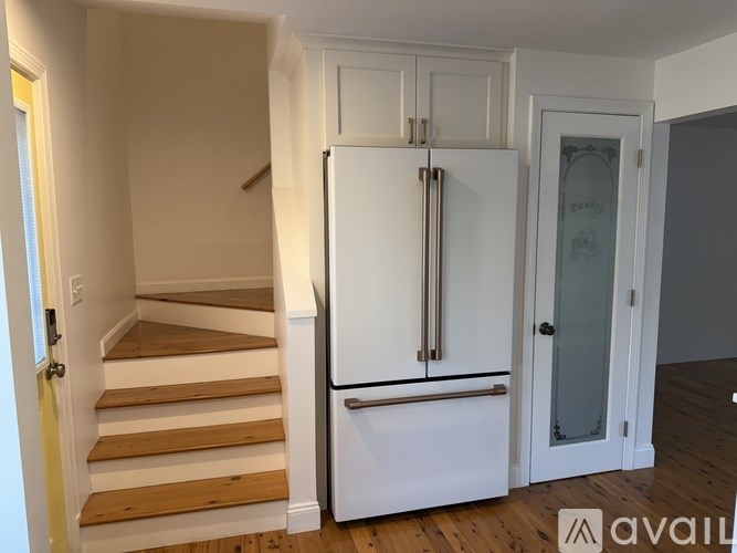 A white refrigerator stands in a kitchen next to a staircase.