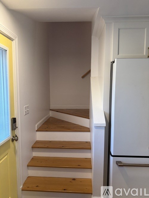 A white refrigerator sits next to a staircase in a room.