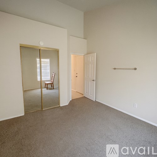 A room with a carpeted floor, a mirror, a door, and a bar.
