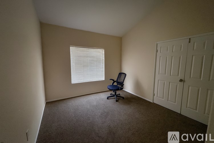 A room with a carpeted floor, a window with blinds, a blue chair, and a white door.