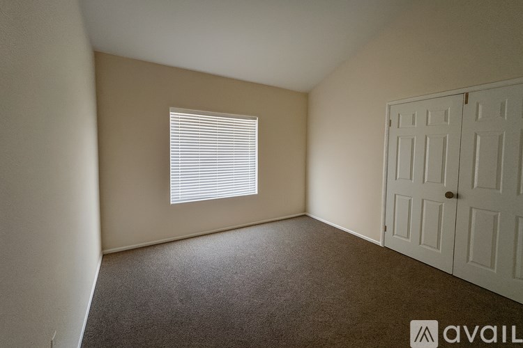 A room with a carpeted floor, a window with blinds, and a white door.
