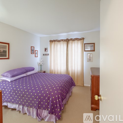 A bedroom with a purple bedspread and a wooden dresser.