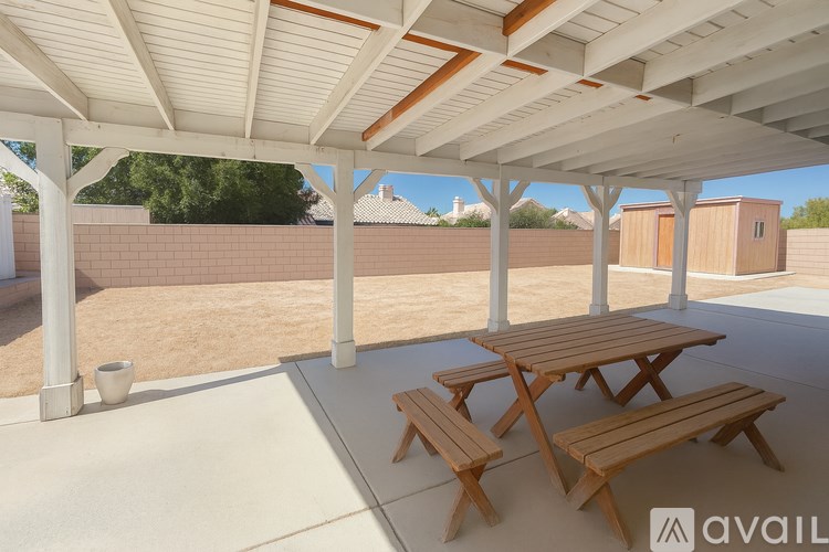 A patio with a table and benches under a roof.