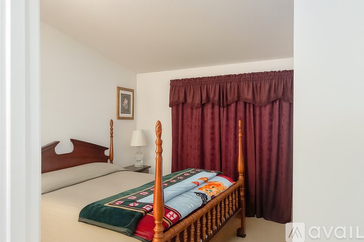 A bedroom with a bed, a nightstand with a lamp, and a picture on the wall.