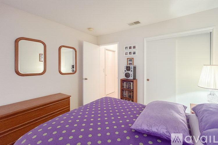 A bedroom with a purple bedspread and two round mirrors on the wall.
