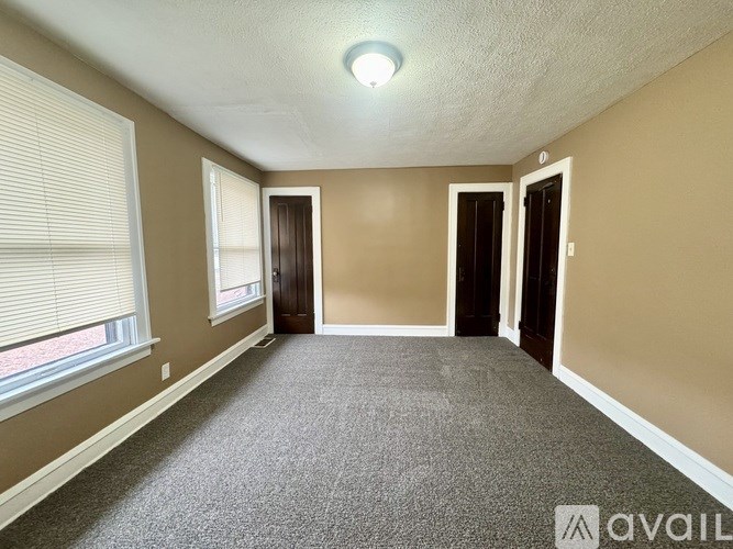 A room with carpeted floor, two doors, and a window with blinds.