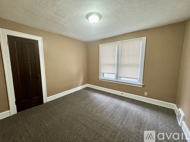 A room with a carpeted floor, a window with blinds, and a door.