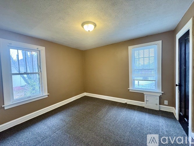 A room with a carpeted floor, a window with blinds, and a ceiling light.