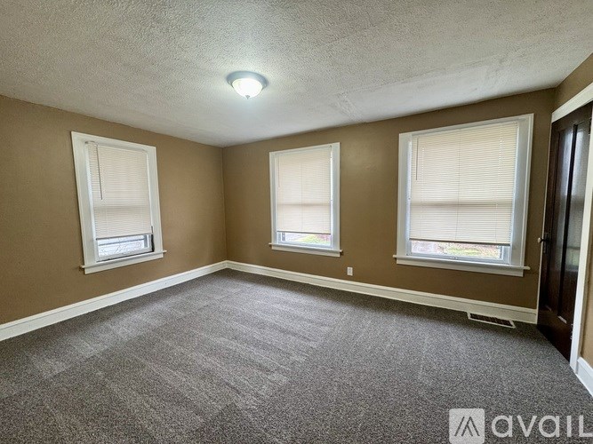 A room with carpeted floor and three windows.