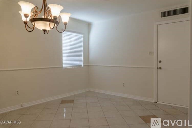 A room with a chandelier, a window with blinds, and a door.