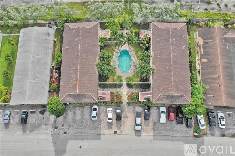 A bird's eye view of a parking lot with cars and a building with a pool in the middle.