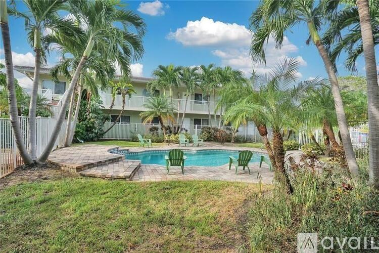 A pool surrounded by palm trees and a white fence.