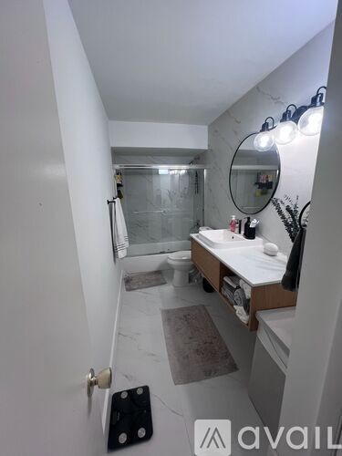 A bathroom with a toilet, sink, mirror, and a rug.