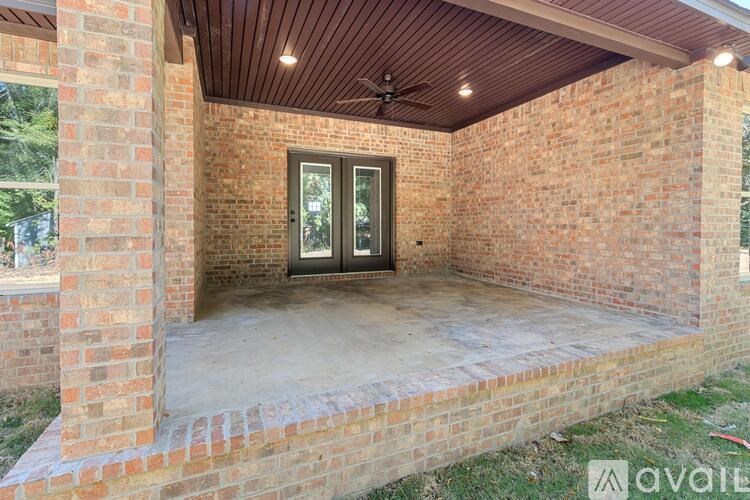 A covered patio area with a ceiling fan and brick walls.