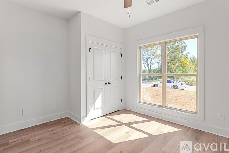A room with a white door and a window with a view of a parking lot and trees.