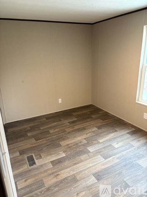 A room with wooden flooring and a window on the right side.