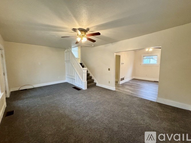 A living room with a carpeted floor and a staircase.