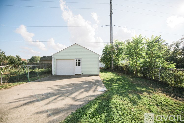 A white garage is situated in a grassy area with a clear sky above.