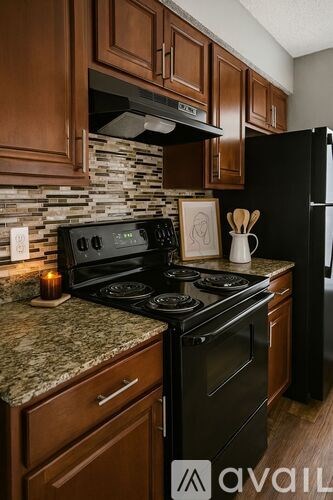 A kitchen with a black refrigerator and a stone backsplash.