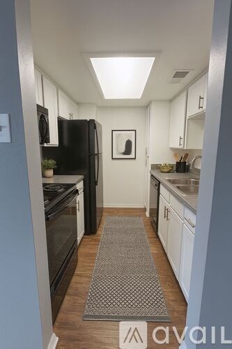 A kitchen with a black refrigerator and a rug on the floor.