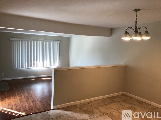 A room with a window covered by blinds, a wooden floor, and a wall with a light switch.