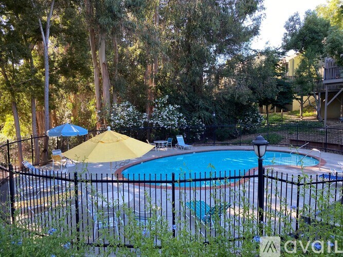 A pool surrounded by a black fence with a yellow umbrella and a blue pool chair.