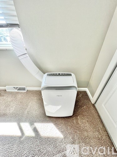 A white portable air conditioner sits on a carpeted floor.