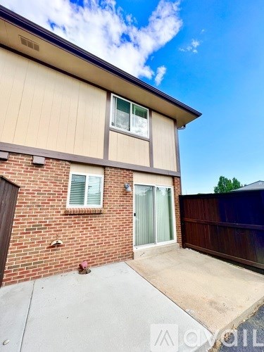 A house with a brown brick wall and a beige siding wall with a sliding glass door.