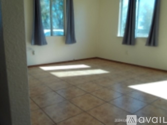 A room with tile flooring and two windows with curtains.