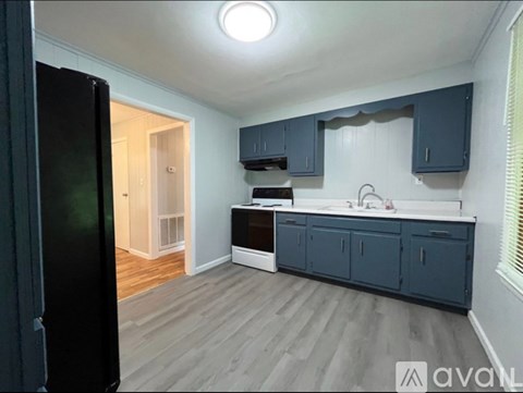 A kitchen with a black refrigerator and wooden flooring.