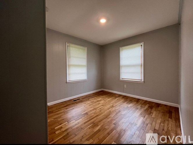 A room with wooden flooring and two windows.