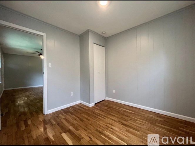 A room with wooden flooring and white walls, with a door and a window.