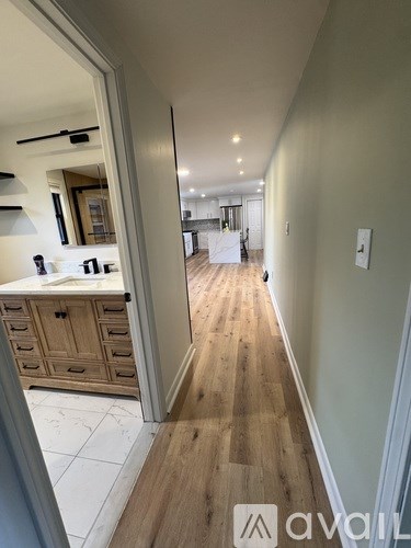 A hallway with a wooden floor leads to a kitchen area.
