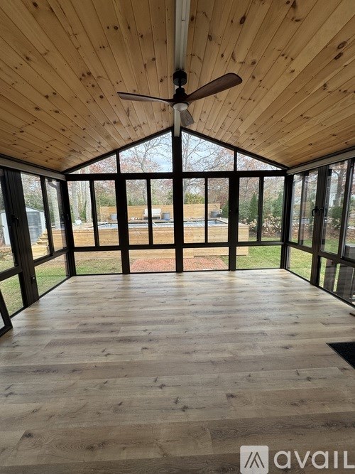 A room with wooden walls and ceiling and a fan in the middle.