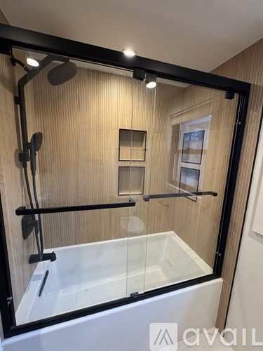 A modern bathroom with a glass shower enclosure and a white bathtub.