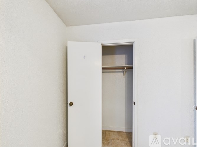 A white door with a gold handle is open to a room with a white wall and a brown floor.