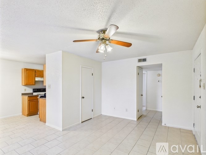 A spacious living room with a kitchen area to the left and a doorway leading to another room to the right.