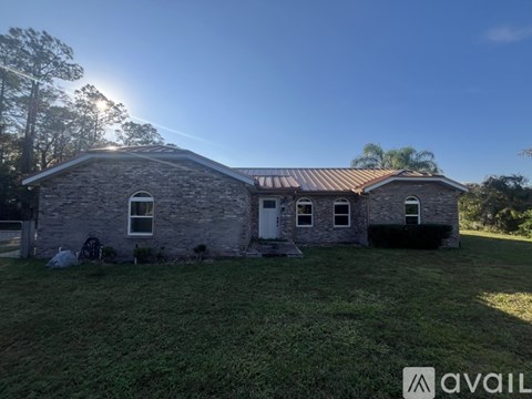 A house with a stone exterior and a metal roof is surrounded by a grassy yard.